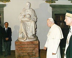 Pope John Paul II on a visit to the Great Historic Hall of the University of Pisa. Above center, a statue of Galileo by Paolo Emilio Demi.