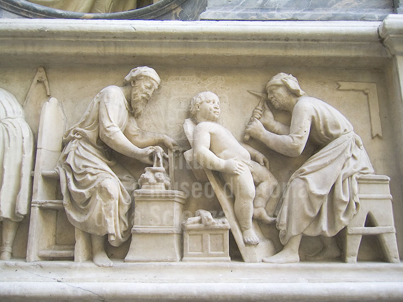 Tabernacle of the Four Crowned Saints, detail of the bas-relief depicting two saints at work:  one, with a compass and square, makes a capital, while the other sculpts a putto with a pick or mattock, Nanni di Banco, 1408, Orsanmichele.